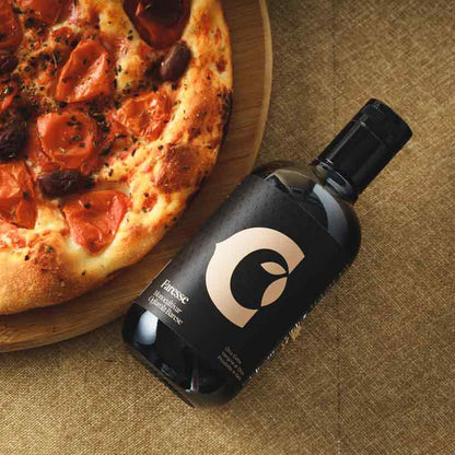 Flasche Olivenöl "Faresse" neben Pizza auf Tisch.