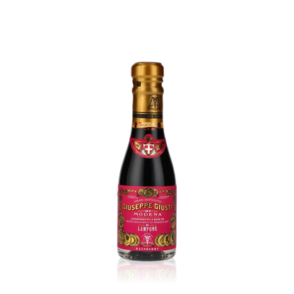 Giuseppe Giusti Himbeer-Balsamessig Flasche vor schwarzem Hintergrund.