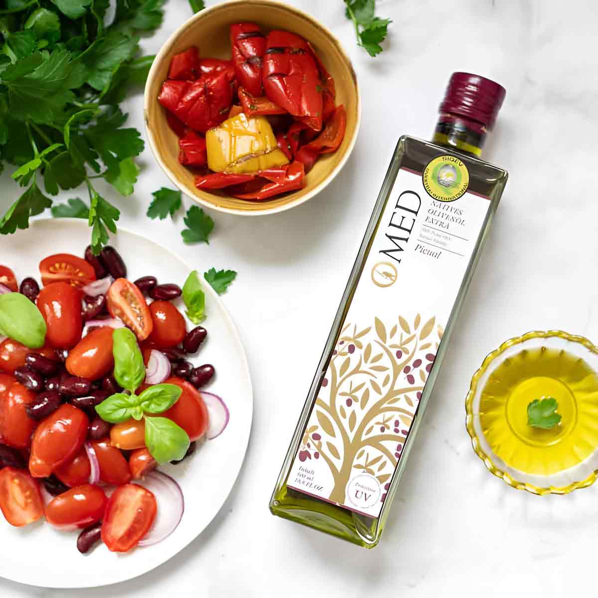 O-MED Olivenölflasche mit Gemüse und Kräutern arrangiert.