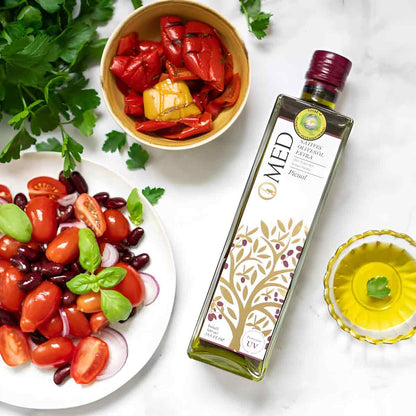 O-MED Olivenölflasche mit Gemüse und Kräutern arrangiert.