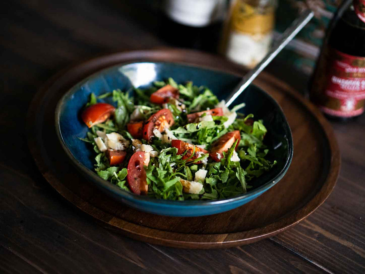 Rucola mit Kirschtomaten,Parmesan und Balsamico-Dressing auf blauem Teller