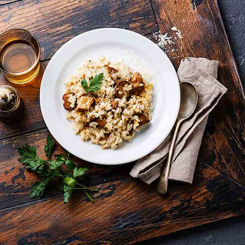 Teller mit Steinpilzrisotto, Petersilie, Glas Wein, Besteck.