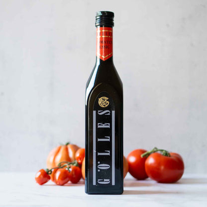 Gölles Tomatenessig Flasche vor frischen Tomaten auf Tisch.