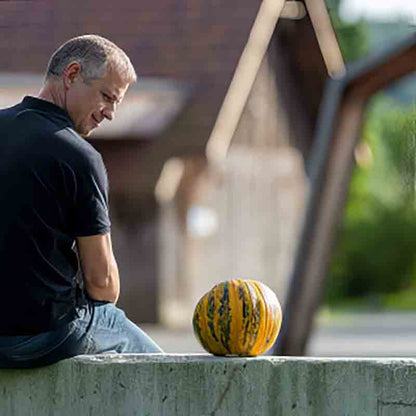 Thomas Hartlieb mit Kürbis auf einer Mauer, den er liebevoll anblickt