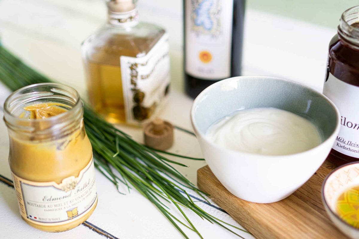 Zutaten für ein Joghurt-Dressing stehen auf einem Tisch. Joghurt, weißer Balsamico, Olivenöl, Honig, Senf, Schnittlauch
