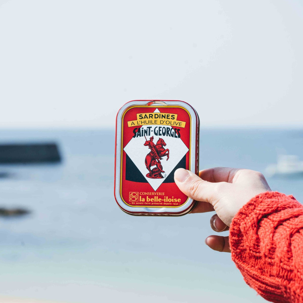 Hand hält Sardinen-Dose von La Belle-Iloise am Meer.