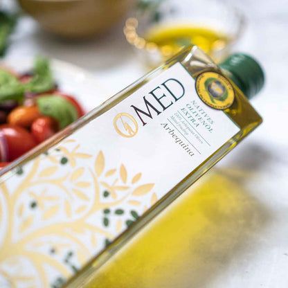O-MED Olivenölflasche liegend, im Hintergrund Tomaten und Basilikum.