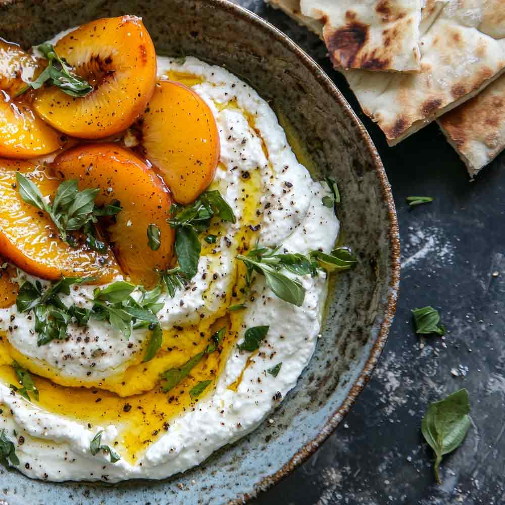 Ricotta mit Olivenöl, Pfirsichen und Kräutern in Schale.