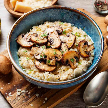 Risotto mit Pilzen in blauer Schüssel, Parmesan daneben.