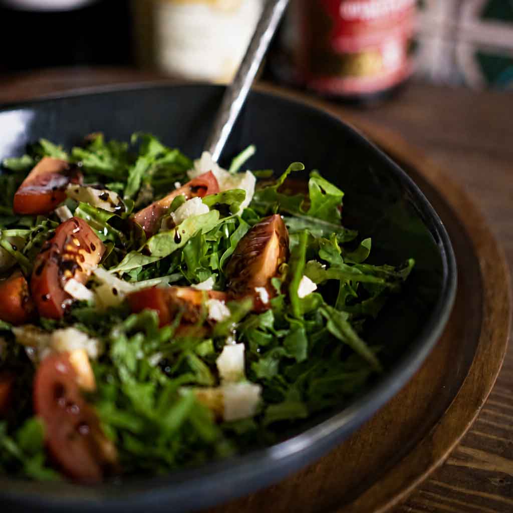 Nahaufnahme von einem Salat aus Rucola, Kirschtomaten, Parmesan und Balsamico